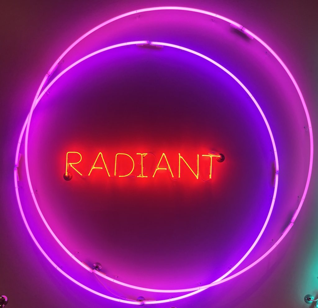 a neon sign. there is are two purple neon circles and inside those circles is the word radiant in red neon