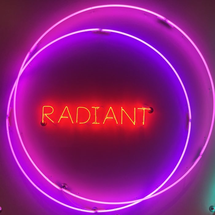 a neon sign. there is are two purple neon circles and inside those circles is the word radiant in red neon