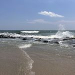 the Atlantic Ocean crashing upon rocks in Ocean City, NJ. The sandy beach is in the foreground