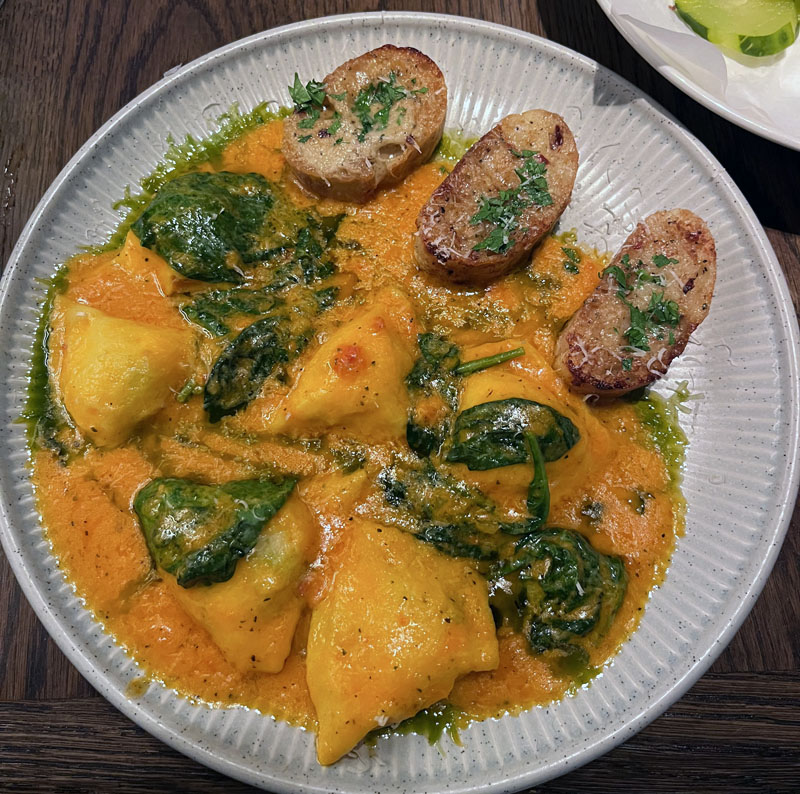 Dinner at Love Restaurant. A plate of ravioli covered in a bright orange sauce and wilted spinach leaves. there are also 3 toasted bread slices.