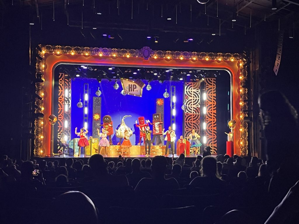 a lit up stage at HersheyPark: on the stage are costumed candy characters and dancers in sparkly costumes
