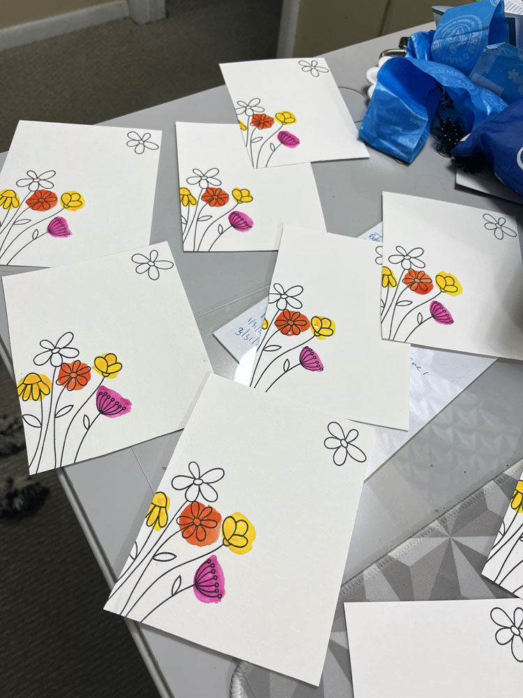 cards in progress: seven cards with tamped flowers with colorful spots of pink, yellow, and orange behind them. Some of the flowers aren't painted yet.
