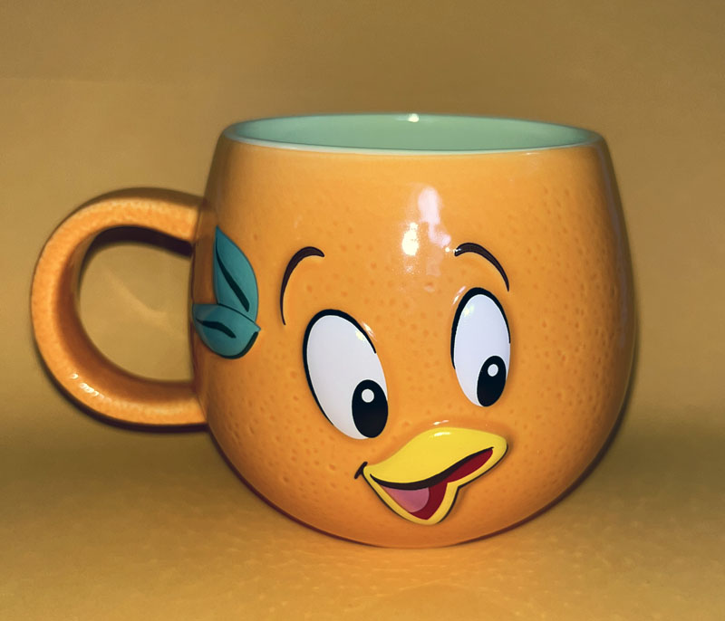 an orange coffee mug with eyes and a yellow bill. the inside is green