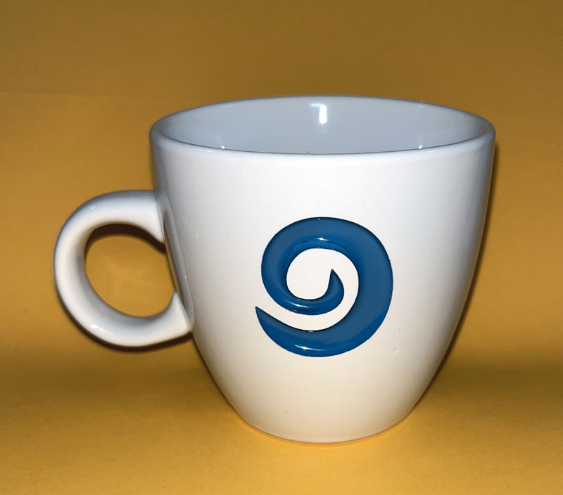 a white mug with a small roundish handle and a turquiose blue swirl on the front that looks like the World of Warcraft hearthstone symbol