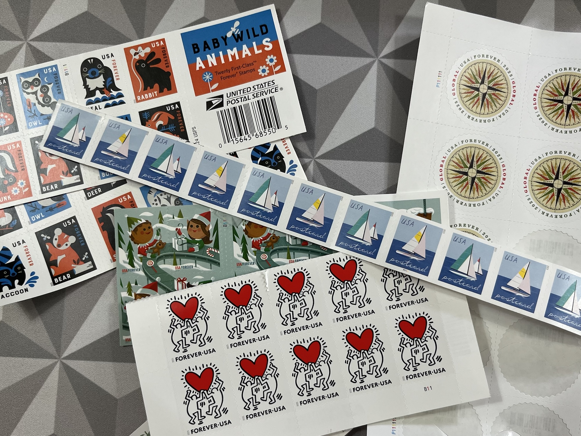 an assortment of US postage stamps. There are Christmas, baby animal, and wildflower stamps for regular postage, international stamps, and a roll of postcard stamps