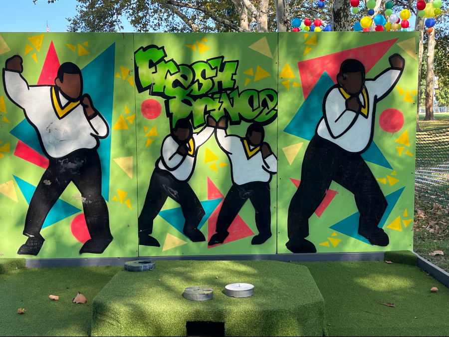 a minigolf hole at The Oval in front of the Philadelphia Art Museum. The backdrop is a graffiti-style wall with FRESH PRINCE on it and four images of Carlton doing his It's not unusual dance.