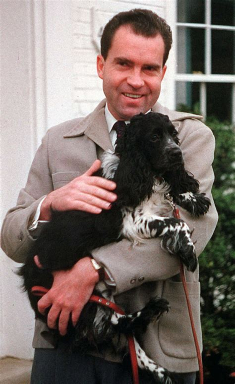 a color photo of Richard Nixon holding his dog Checkers, a black spaniel with white smudges