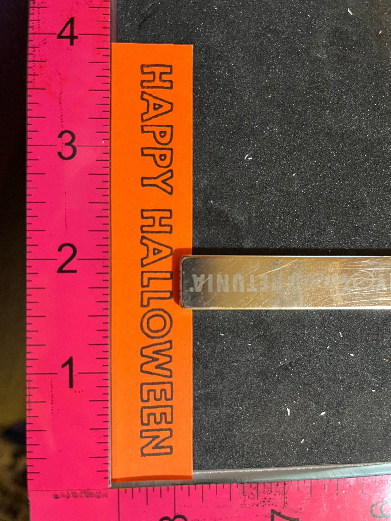 a "HAPPY HALLOWEEN" sentiment stamped on orange cardstock, on a stamping tool
