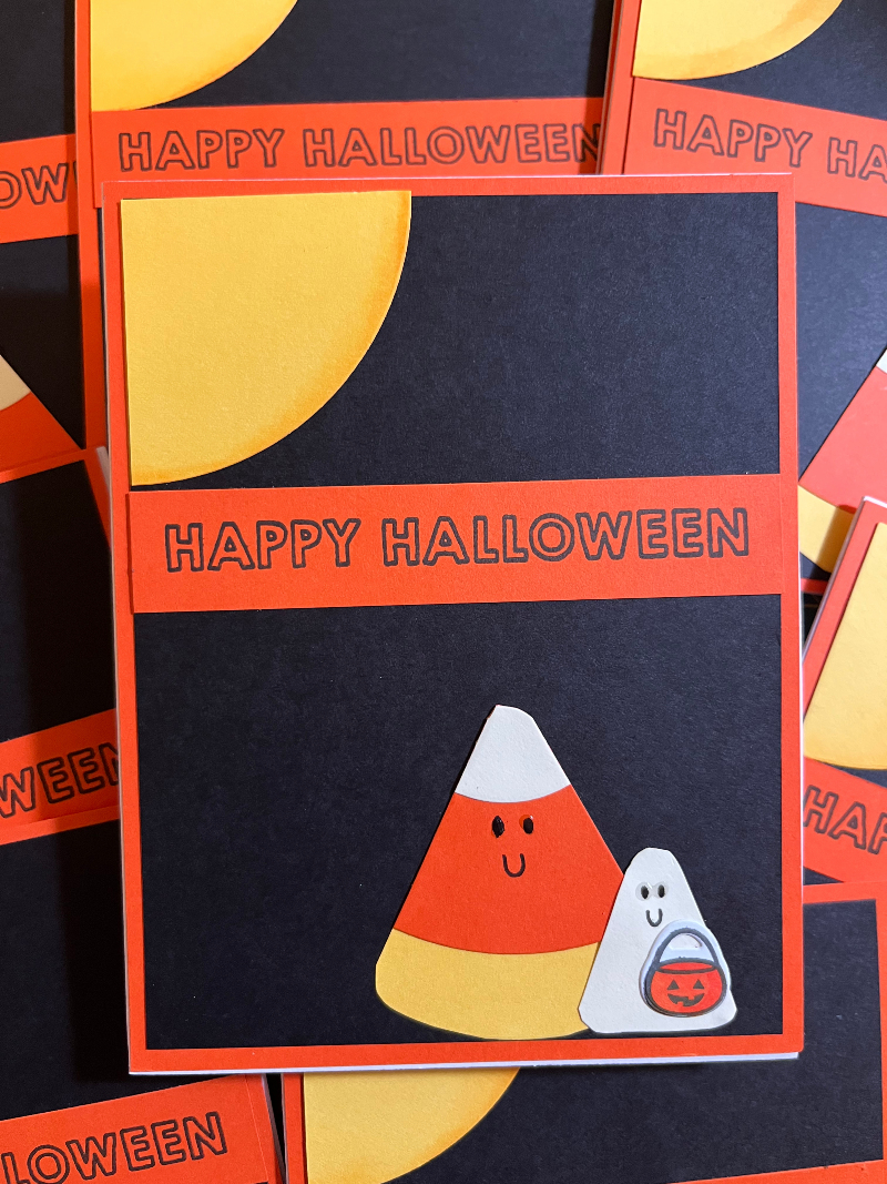 a card front: there is a moon in the upper left corner, a HAPPY HALLOWEEN greeting a third of the way down, and at the bottom two figures: one is a smiling candy corn; the other is a ghost with a pumpkin