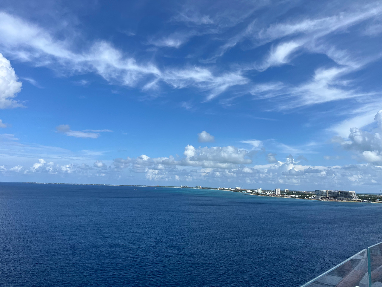shot from a cruise ship. The top 2/3 is blue sky, the bottom 1/3 is blue water, at the left is Grand Cayman from a distance