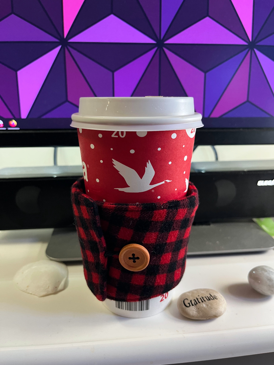 a wawa coffee cup with a buffalo check mug cozy wrapped around it, fastened with a button.