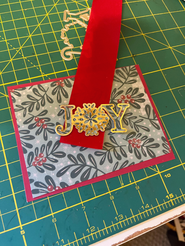 a red and green card with red ribbon and a gold JOY cutout