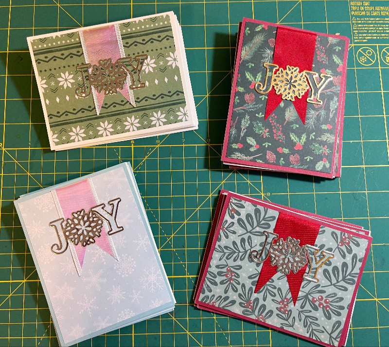 four variations of the same JOY holiday card; one in green, two in red and green, one in blue and white