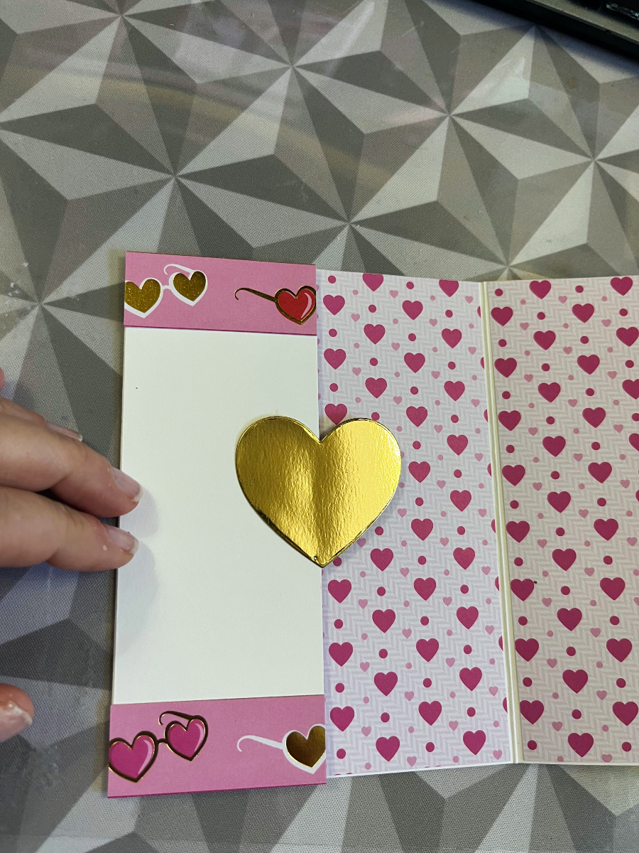 a card with a gold heart and pink paper inside