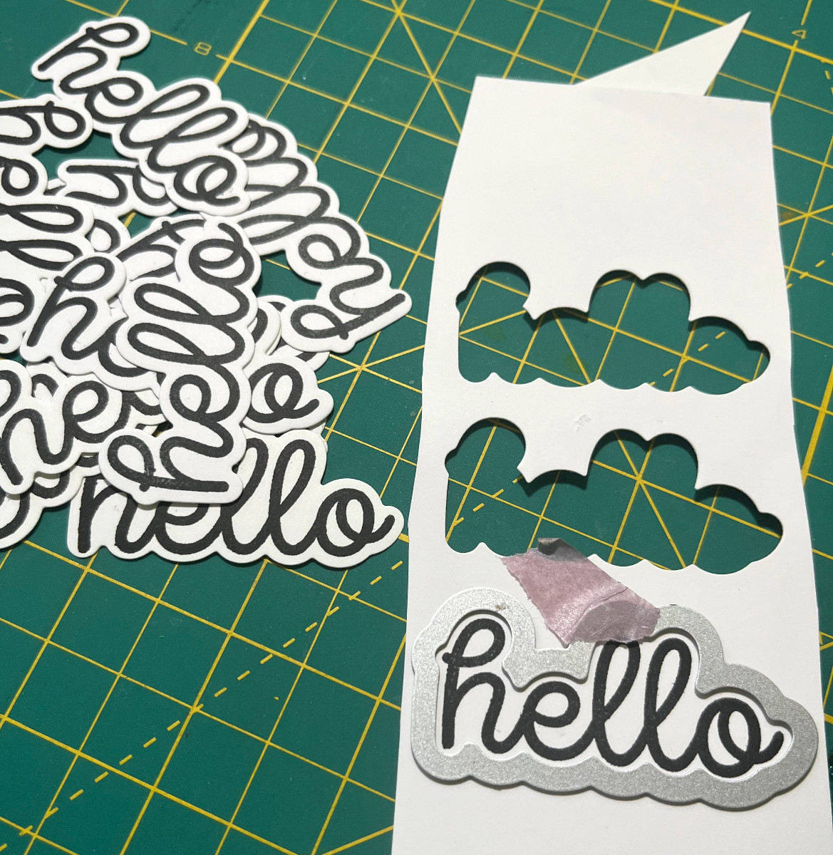 a pile of cut out hellos and a metal die taped around a stamped hello