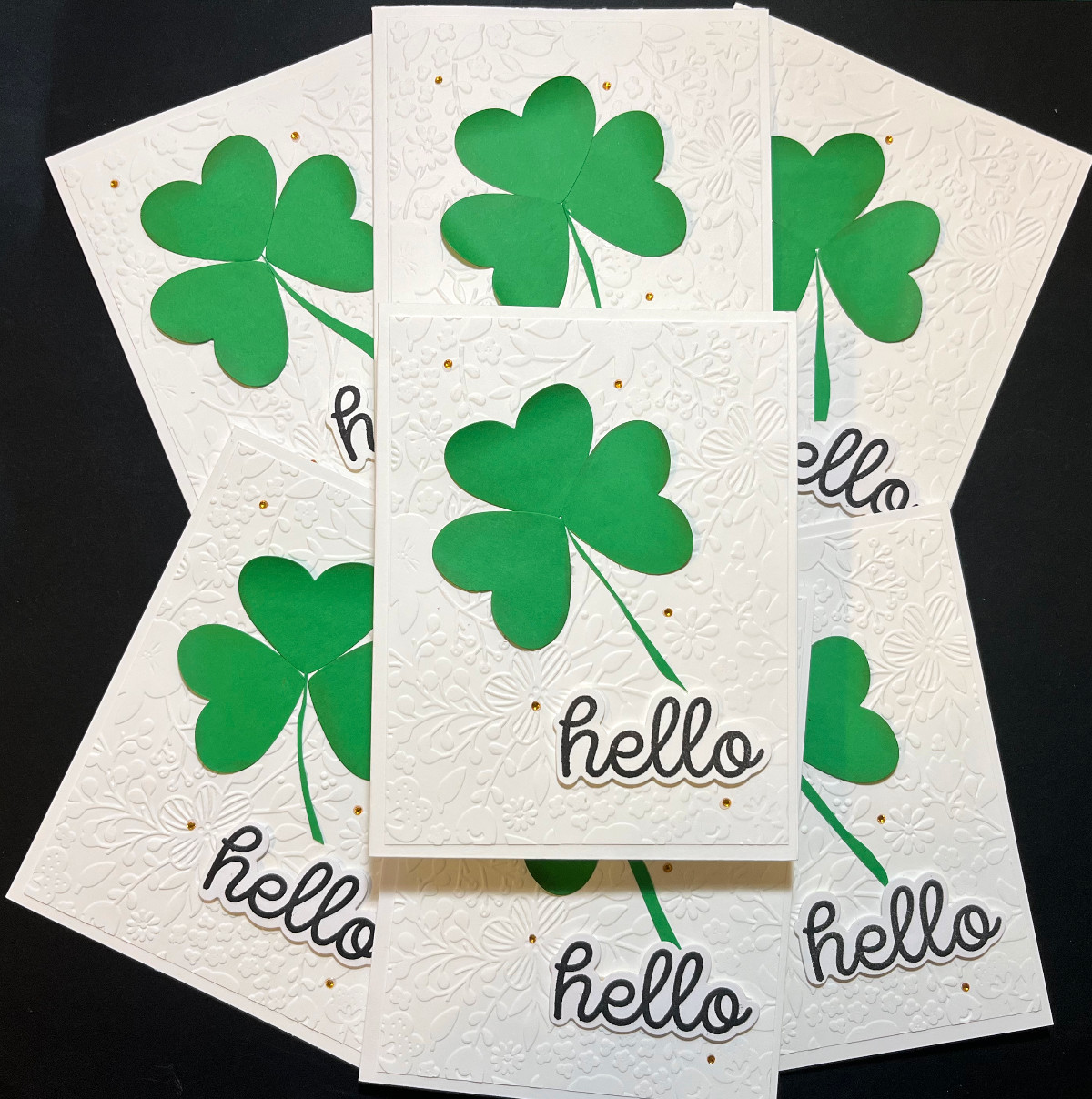 a pile of handmade cards, white embossed background with a paper shamrock on the front and a "hello" sentiment.