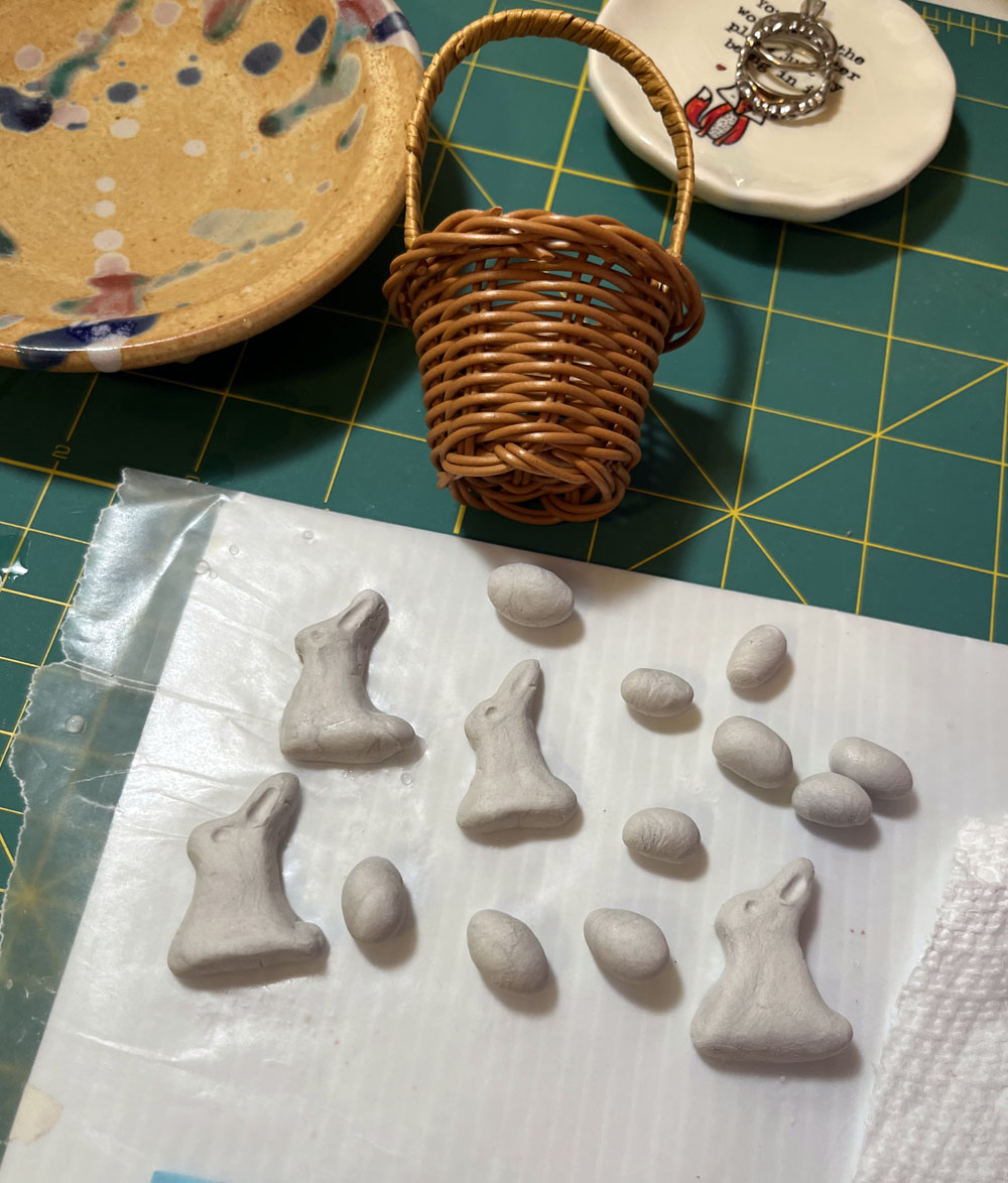 an assortment of clay bunnies and eggs with a small woven basket to determine scale