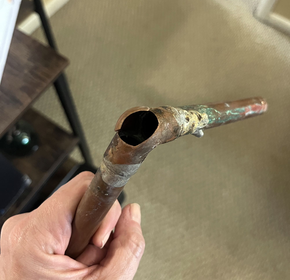 kim holding a copper pipe consisting of two pikes soldered together at a 90 degree joint. There is a hole in the corner of the joint. This, friends, is a burst pipe.