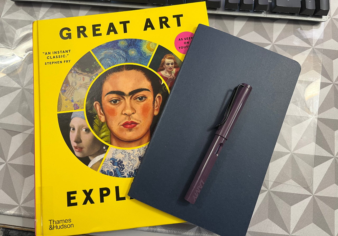 the cover of the book Great Art Explained with a blue notebook and purple fountain pen on it.