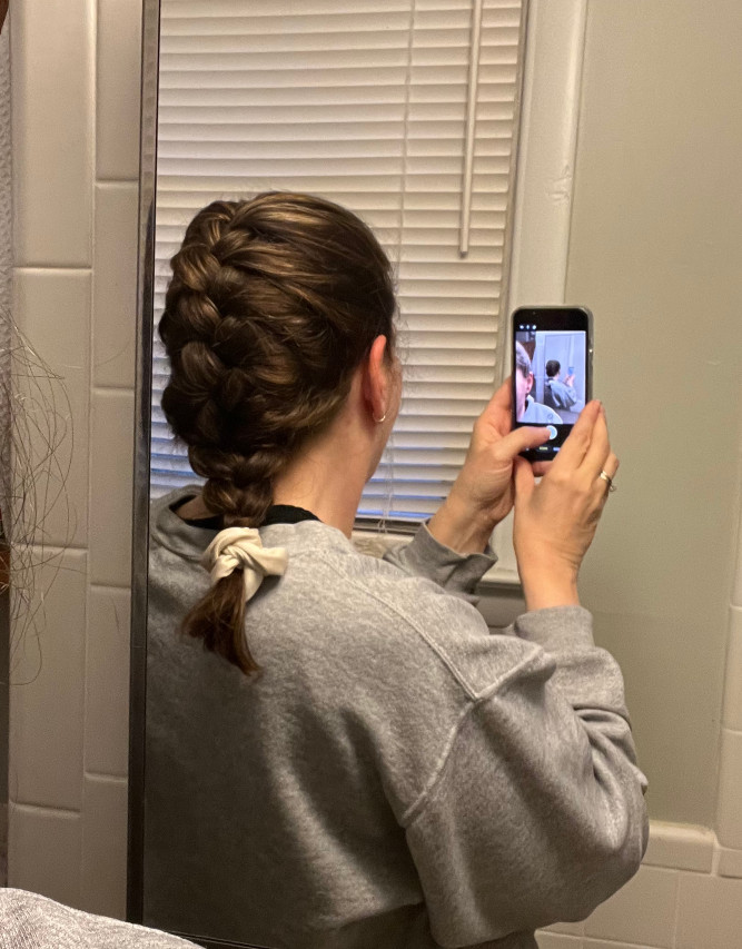 The back of Kim's head, which is French braided surprisingly well. She is holding her mobile phone in selfie mode, which is how she took the photo