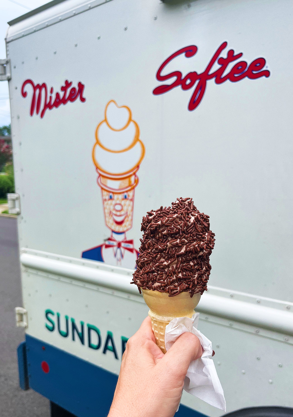 Kim holding a chocolate cone with chocolate jimmies in front of the Mister Softee truck